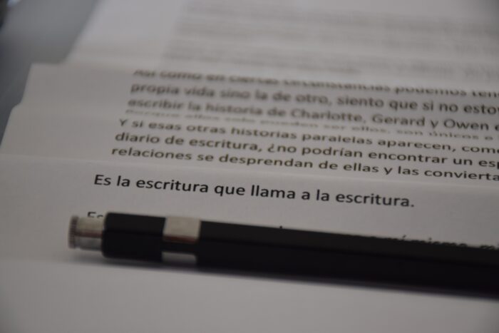 Páginas con “Es la escritura…” y lápiz en primer plano.