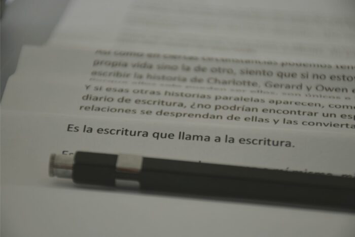 Páginas con “Es la escritura…” y lápiz en primer plano.