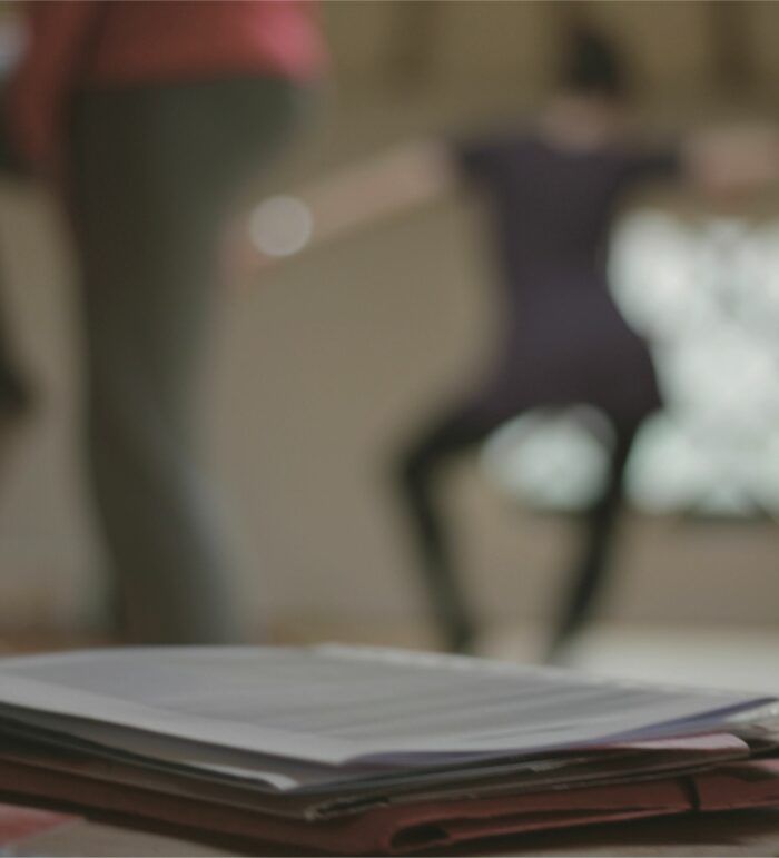 Papeles en primer plano y movimiento al fondo: escritura y danza.