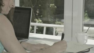 Claudia Mendizábal escribiendo en un cuaderno frente a su computadora