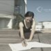 Mujer en movimiento escribiendo en una libreta mientras realiza una postura de estiramiento en el suelo; la distorsión de la imagen transmite dinamismo entre cuerpo y escritura.